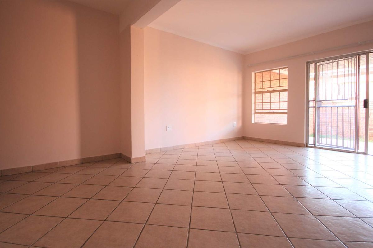 An empty, tiled living area featuring a sliding glass door with a security gate and windows with security bars.