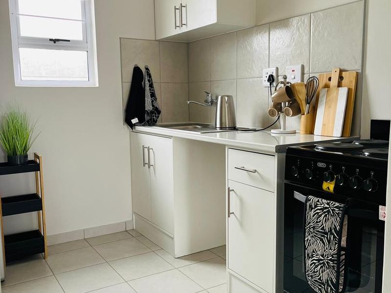A clean and functional kitchen featuring white cabinetry, tiled backsplash, stainless steel sink, and a black freestanding oven.