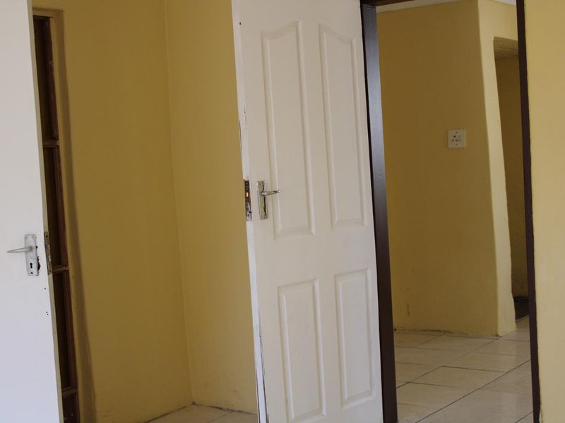 A vacant hallway featuring tiled flooring and internal doors, showing signs of wear on the paintwork and door frames.