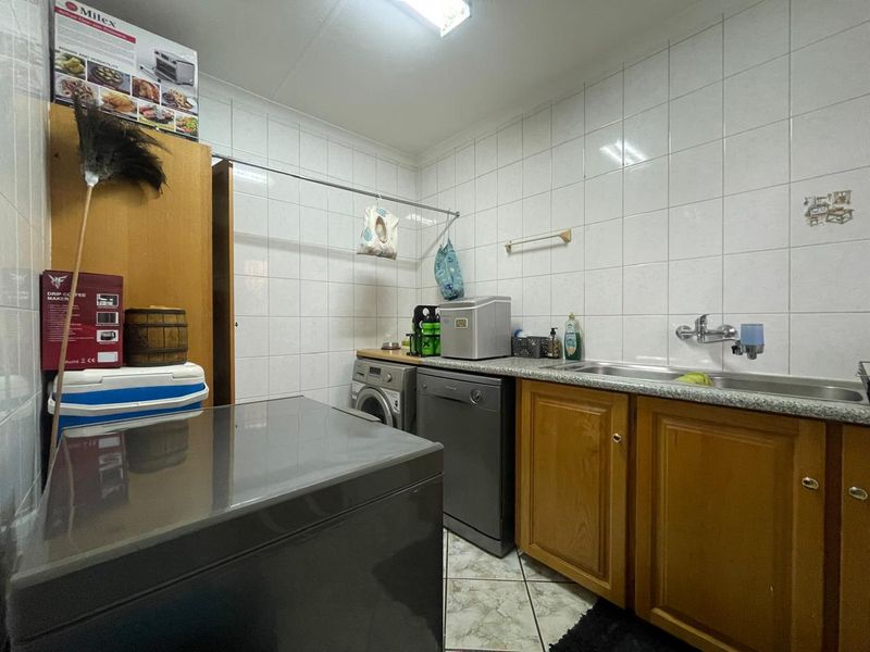 Functional laundry room featuring tiled walls, built-in wooden cabinetry, and a stainless steel sink with plumbing connections for appliances.