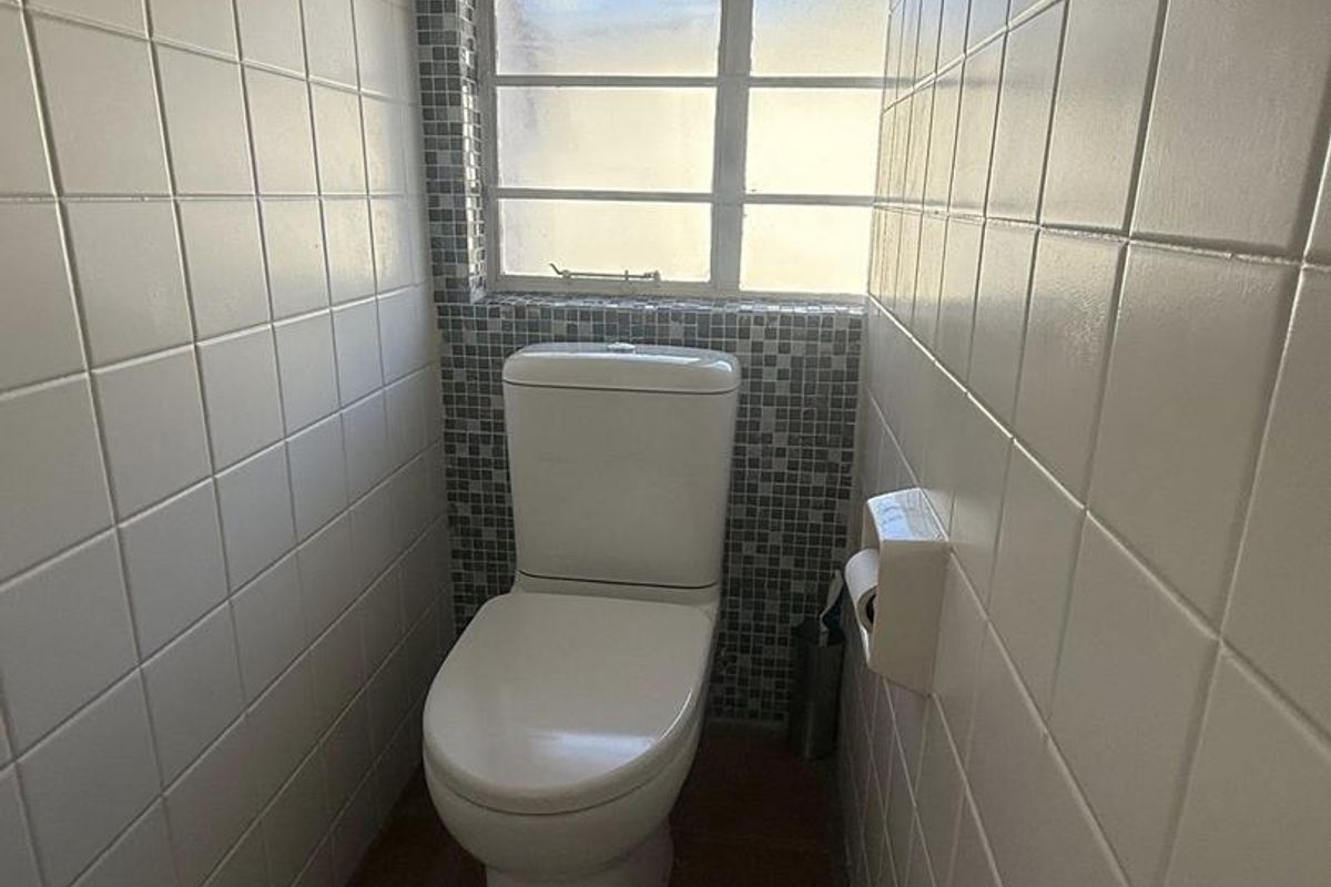 A compact bathroom featuring white wall tiles, mosaic accent tiling around the window, and a standard white toilet suite.