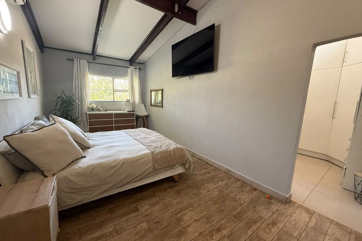 A well-lit bedroom featuring exposed timber ceiling beams, tiled flooring, and convenient access to an adjoining dressing area with built-in cupboards.