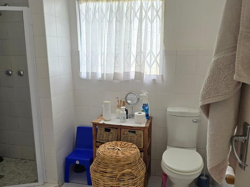 A functional bathroom featuring a shower enclosure, white wall tiles, and tiled flooring, equipped with a standard toilet and a security-fitted window.