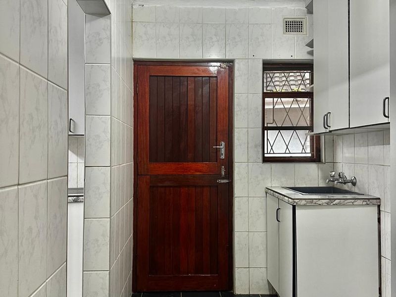 A functional scullery area featuring built-in cabinetry, a sink, tiled finishes, and a solid timber door leading to the exterior.