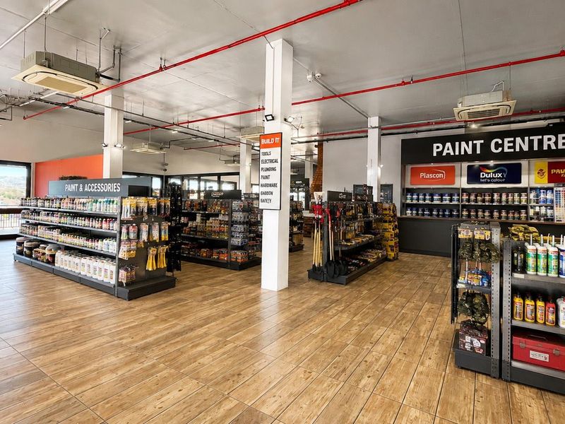 Spacious retail interior featuring wood-look tile flooring, exposed fire suppression systems, ceiling-mounted climate control, and organized built-in shelving for paint and hardware products.