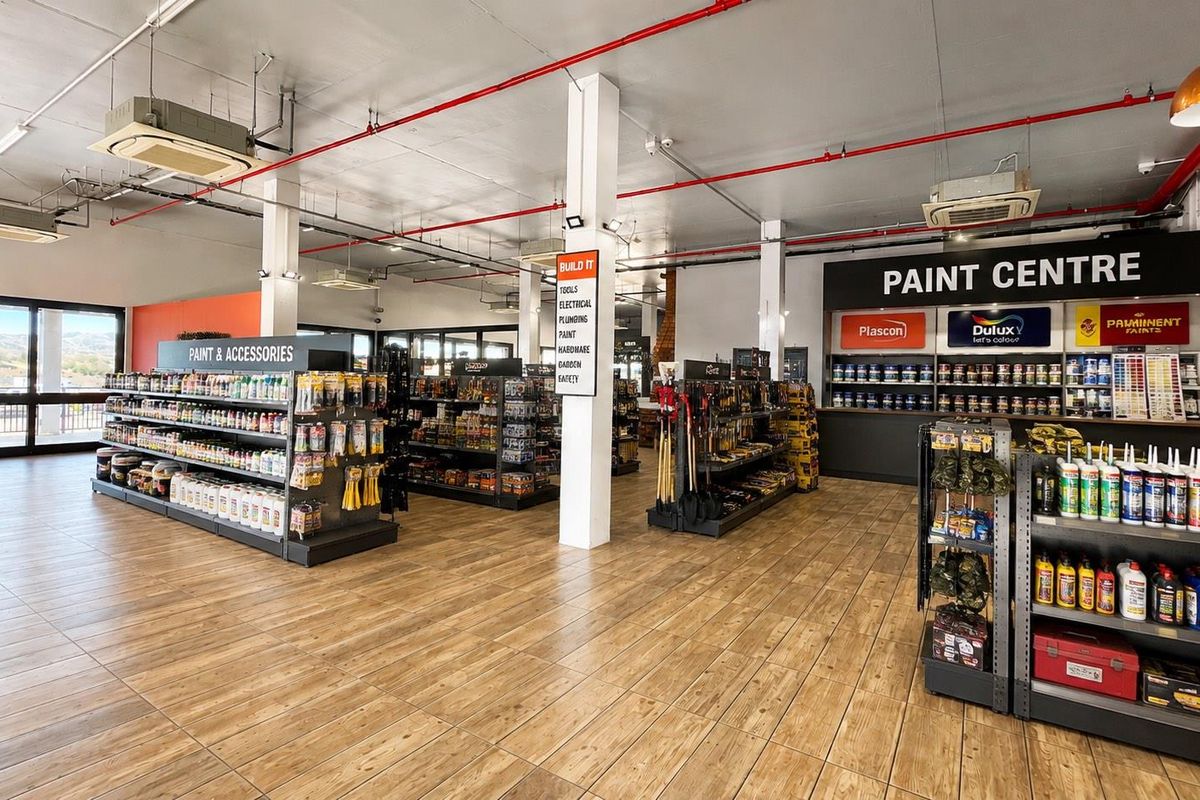 Spacious retail interior featuring wood-look tile flooring, exposed fire suppression systems, ceiling-mounted climate control, and organized built-in shelving for paint and hardware products.