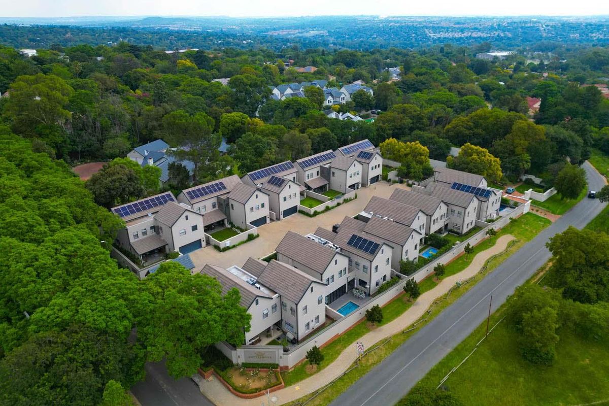 Aerial view of a modern residential complex featuring multiple townhouses with tiled roofs, solar panels, and private swimming pools in a lush green setting.