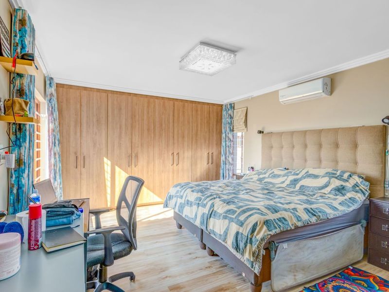 A well-maintained bedroom featuring extensive built-in wooden cupboards, laminate flooring, and a wall-mounted air conditioning unit for climate control.
