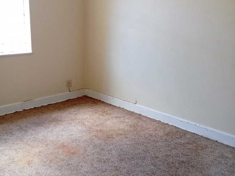 An empty bedroom featuring worn, stained carpeting and dated light fixtures, requiring cosmetic updates to improve the overall condition.