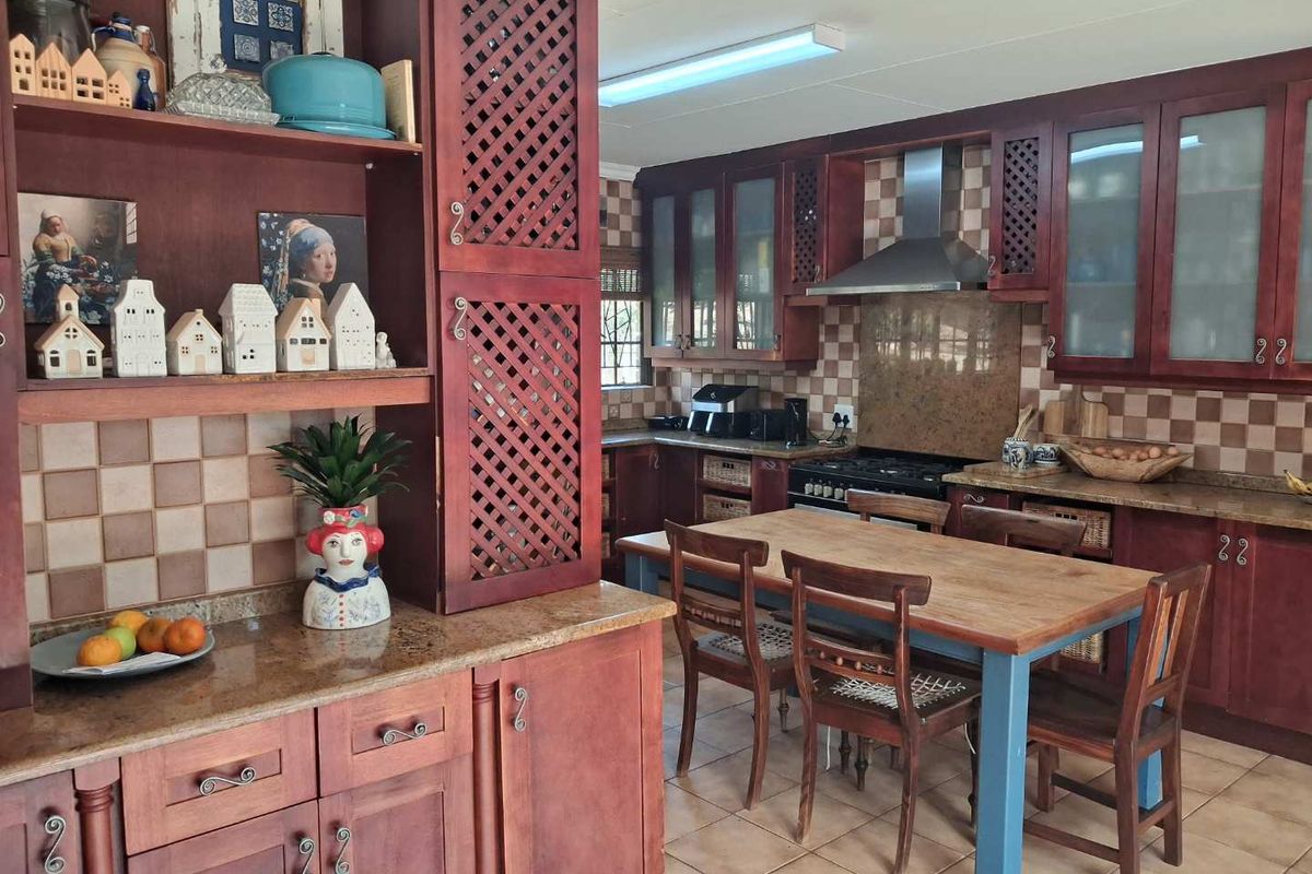 A traditional kitchen featuring dark wood cabinetry, granite countertops, a gas hob with extractor fan, and tiled flooring with an integrated dining area.