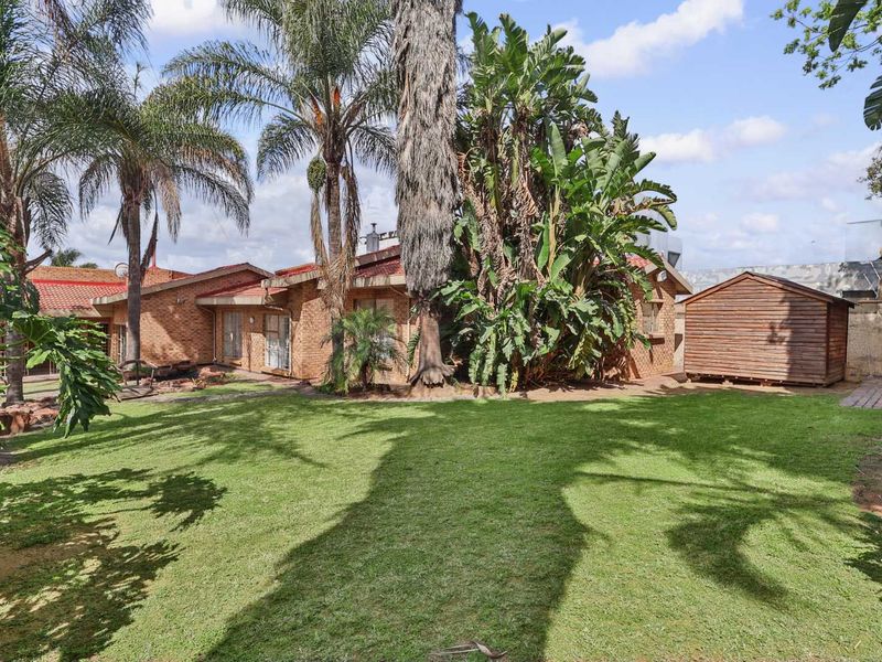 A spacious rear garden featuring a well-maintained lawn, mature landscaping, and a detached wooden storage shed adjacent to the brick house exterior.