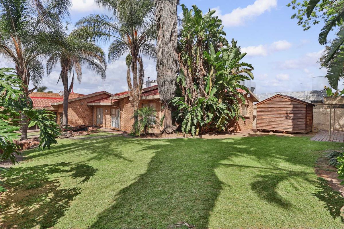 A spacious rear garden featuring a well-maintained lawn, mature landscaping, and a detached wooden storage shed adjacent to the brick house exterior.