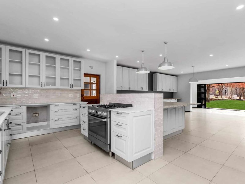 Spacious open-plan kitchen and living area featuring modern white cabinetry, a central island with gas stove, tiled floors, and large sliding doors to the garden.