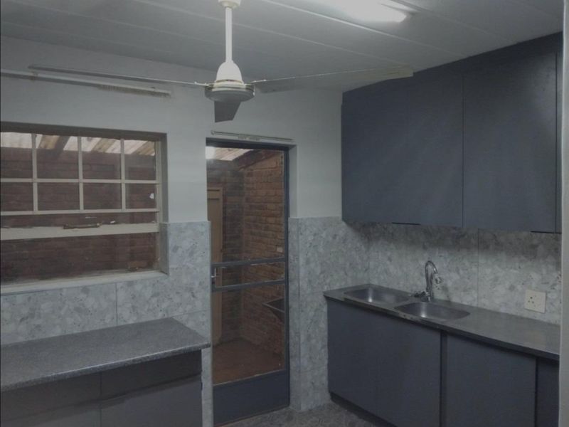 A functional kitchen featuring dark cabinetry, double stainless steel sink, tiled splashbacks, and direct access to an outdoor area.