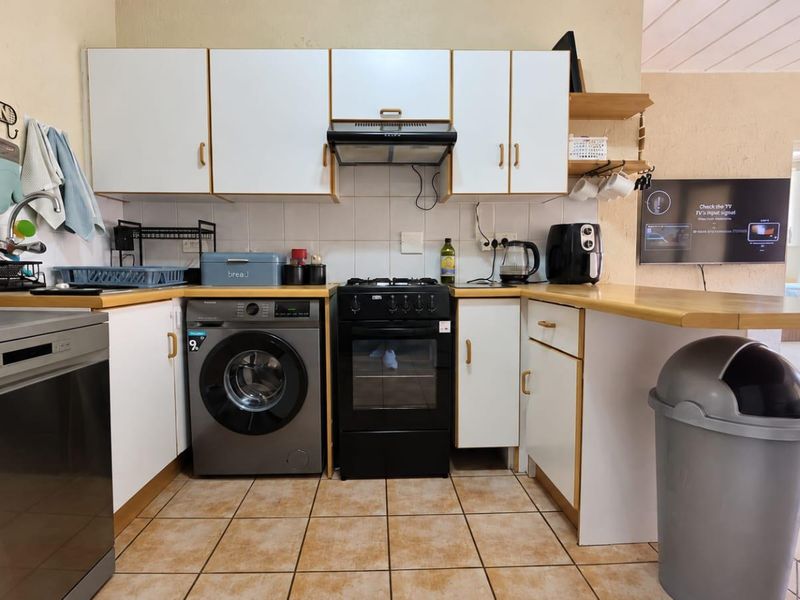 A functional kitchen featuring white cabinetry, laminate countertops, a tiled backsplash, and a freestanding oven, with an open-plan layout connecting to the living area.
