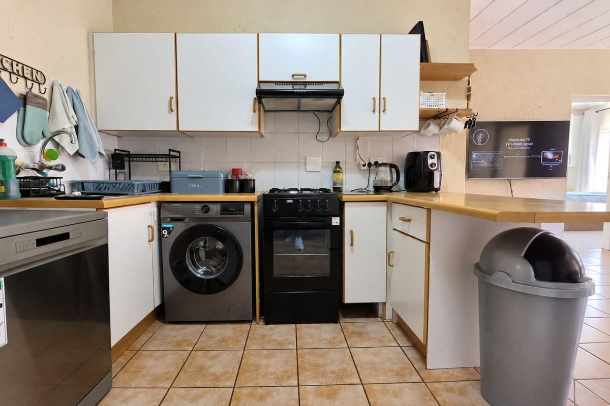 A functional kitchen featuring white cabinetry, laminate countertops, a tiled backsplash, and a freestanding oven, with an open-plan layout connecting to the living area.