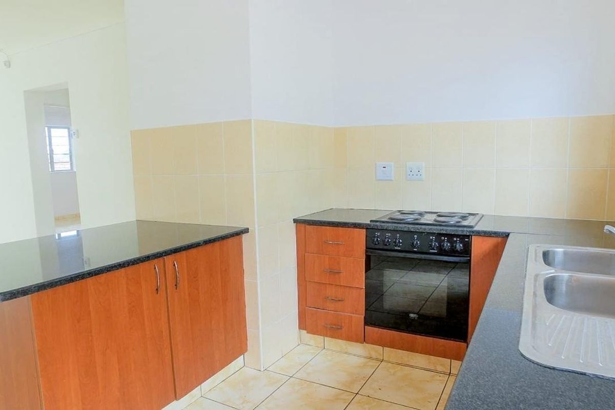 A functional kitchen featuring wooden cabinetry, granite countertops, a built-in oven with electric hob, and a double stainless steel sink.