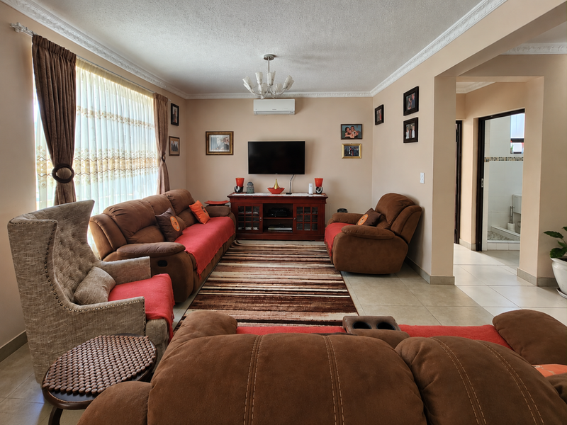 A comfortable living room featuring tiled flooring, decorative ceiling coving, and a wall-mounted air conditioning unit, with an adjacent view into a bathroom area.