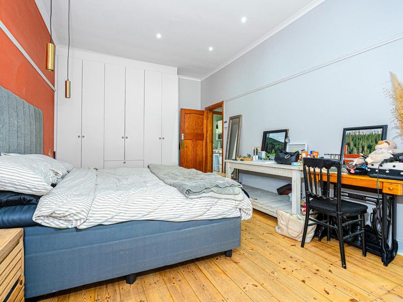 A well-lit bedroom featuring polished timber flooring, built-in white wardrobes, and a decorative picture rail, offering a comfortable and functional living space.