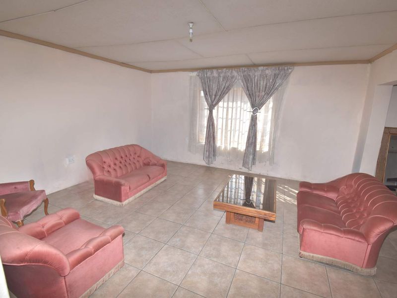 A living room featuring tiled flooring, security bars on the window, and a drop ceiling with visible wear.