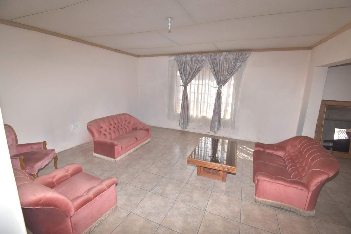 A living room featuring tiled flooring, security bars on the window, and a drop ceiling with visible wear.