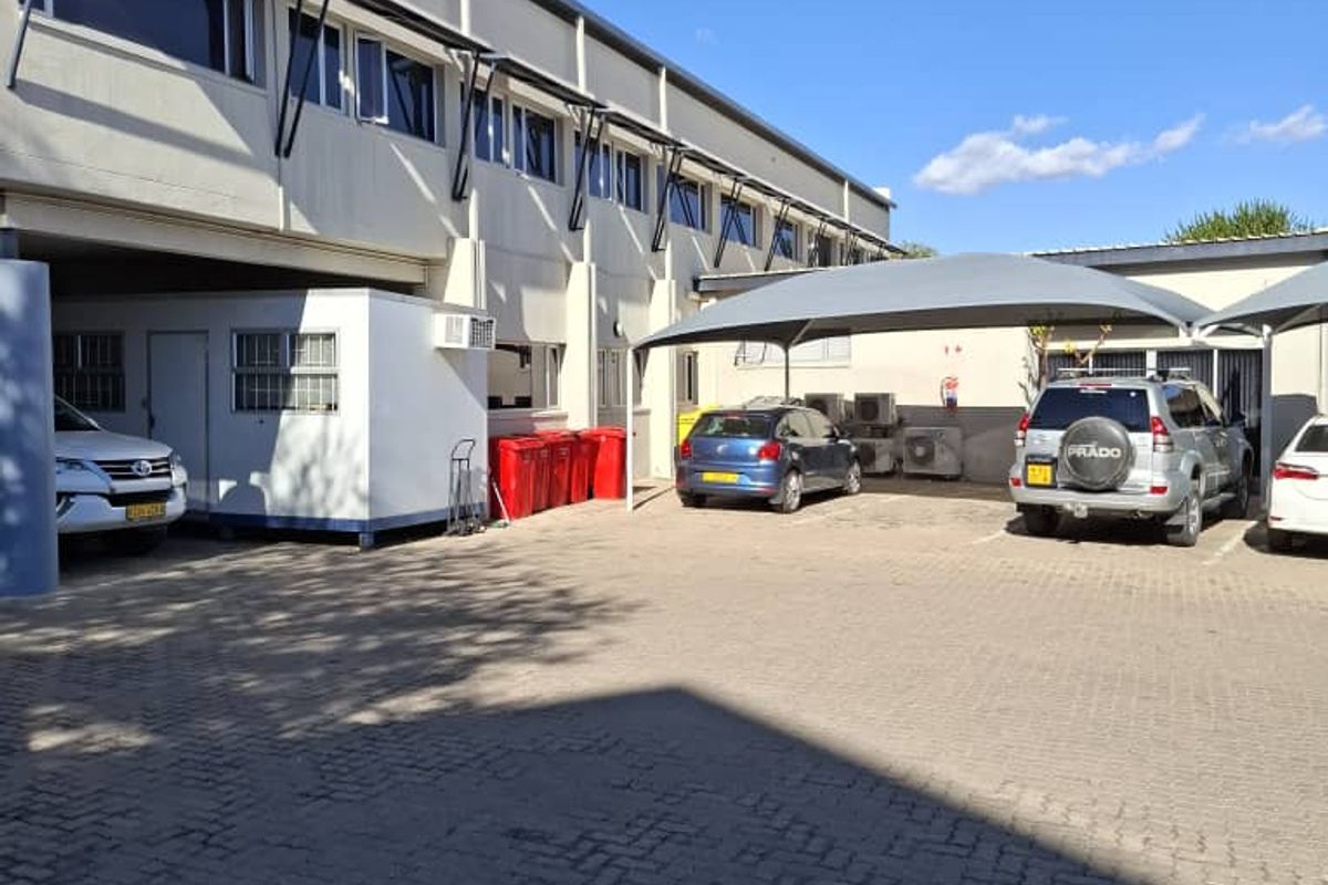Exterior view of the office building featuring a paved parking area with shade cloth carports and multi-level office windows.