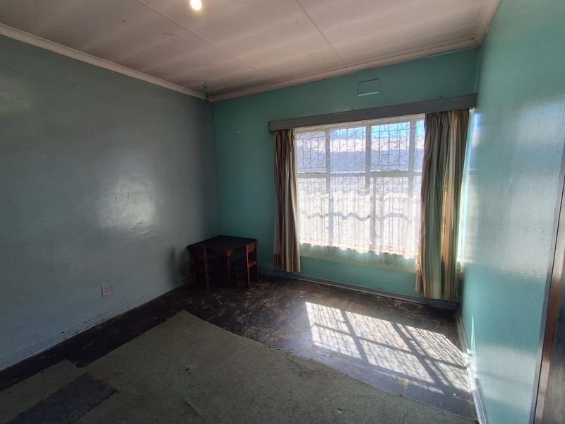A vacant bedroom featuring a large window, coved ceiling, and worn flooring, offering a blank canvas for renovation and modernization.