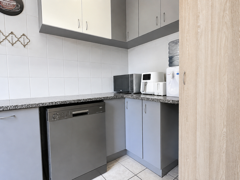 A functional scullery featuring modern grey cabinetry, granite countertops, tiled backsplash, and integrated dishwasher, providing efficient additional workspace and storage.