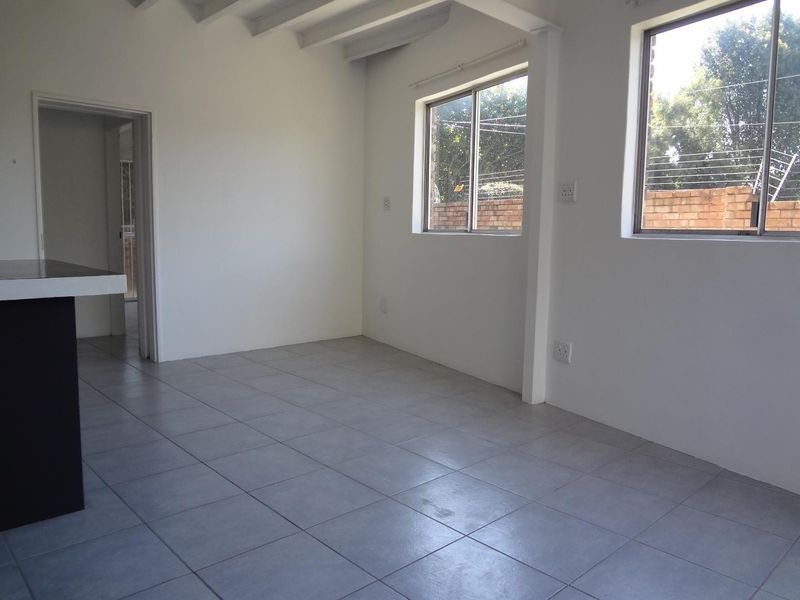 Bright and spacious open-plan living area featuring neutral ceramic floor tiles, exposed timber ceiling beams, and large windows allowing for ample natural light.