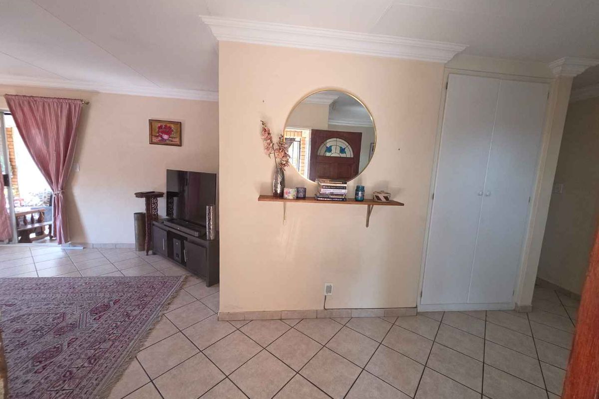 A living area featuring tiled flooring, coving, and a built-in storage cupboard, providing a functional and neutral space.