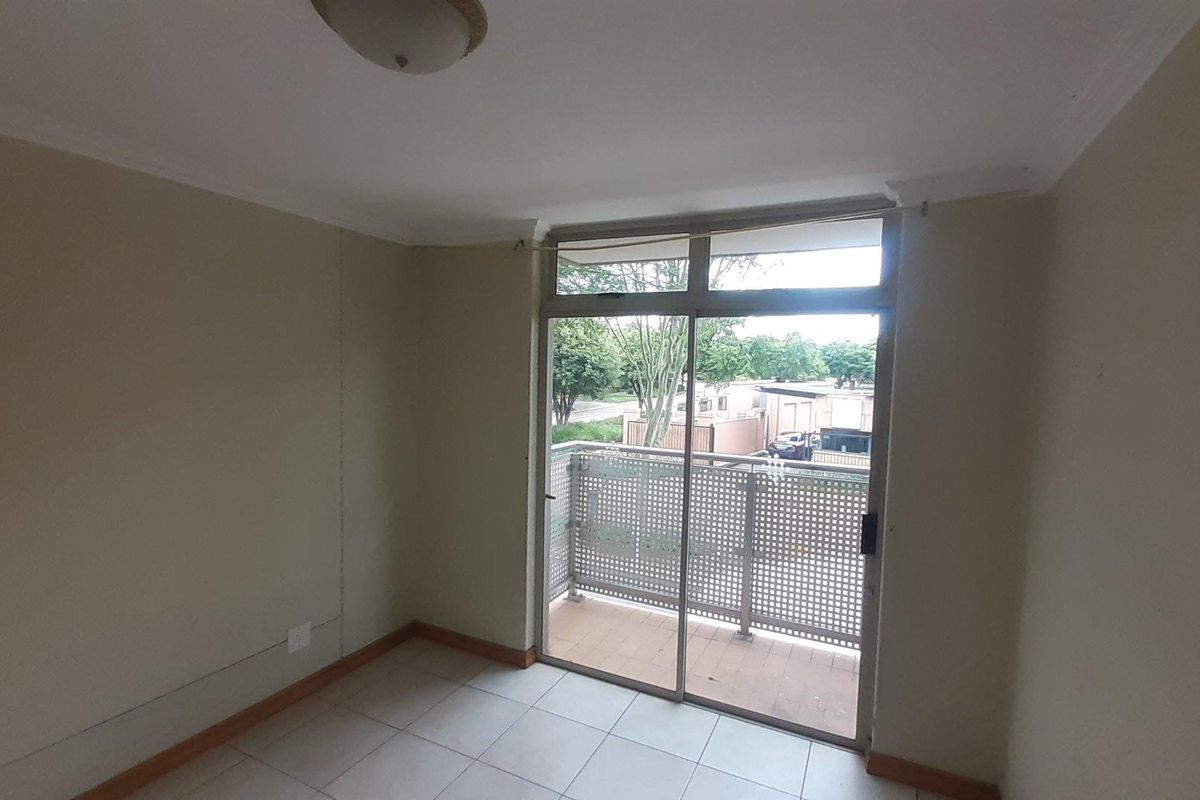An empty bedroom featuring tiled flooring, a ceiling light fixture, and a sliding glass door providing access to a private balcony.