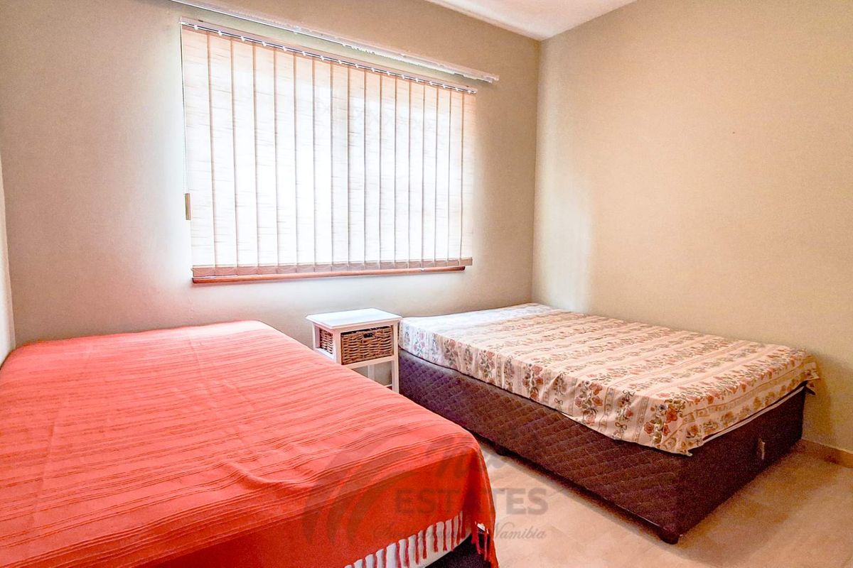 A functional bedroom featuring tiled flooring and vertical window blinds, providing a neutral space ready for personalization.