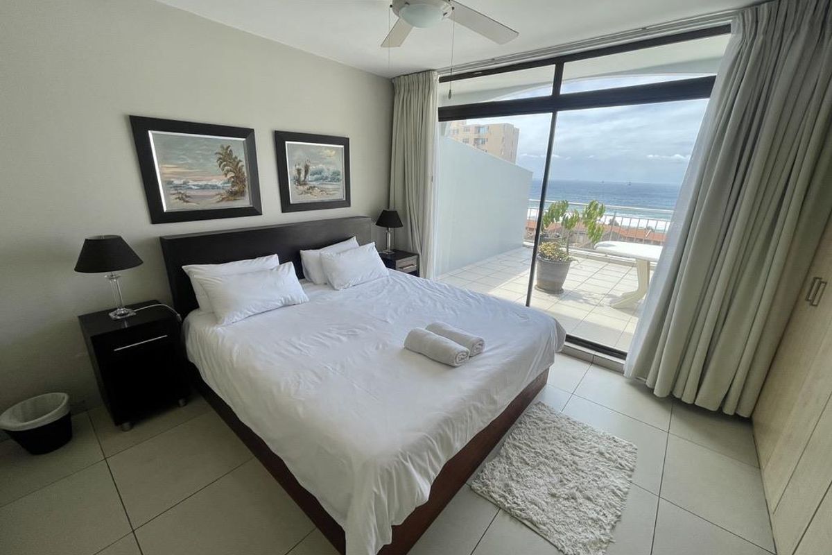 Spacious bedroom featuring large sliding glass doors leading to a private balcony with ocean views, tiled flooring, and built-in cupboards.