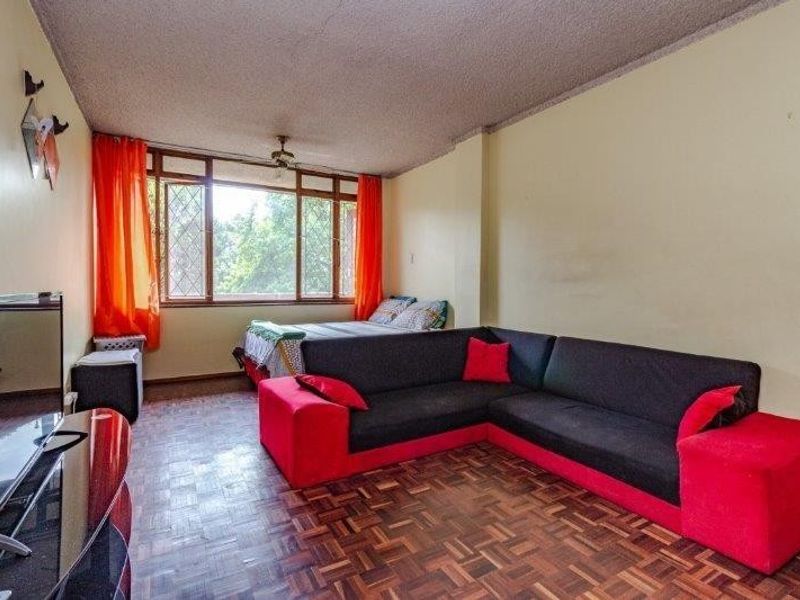 Open-plan living and sleeping area featuring parquet flooring, a ceiling fan, and large windows providing natural light.