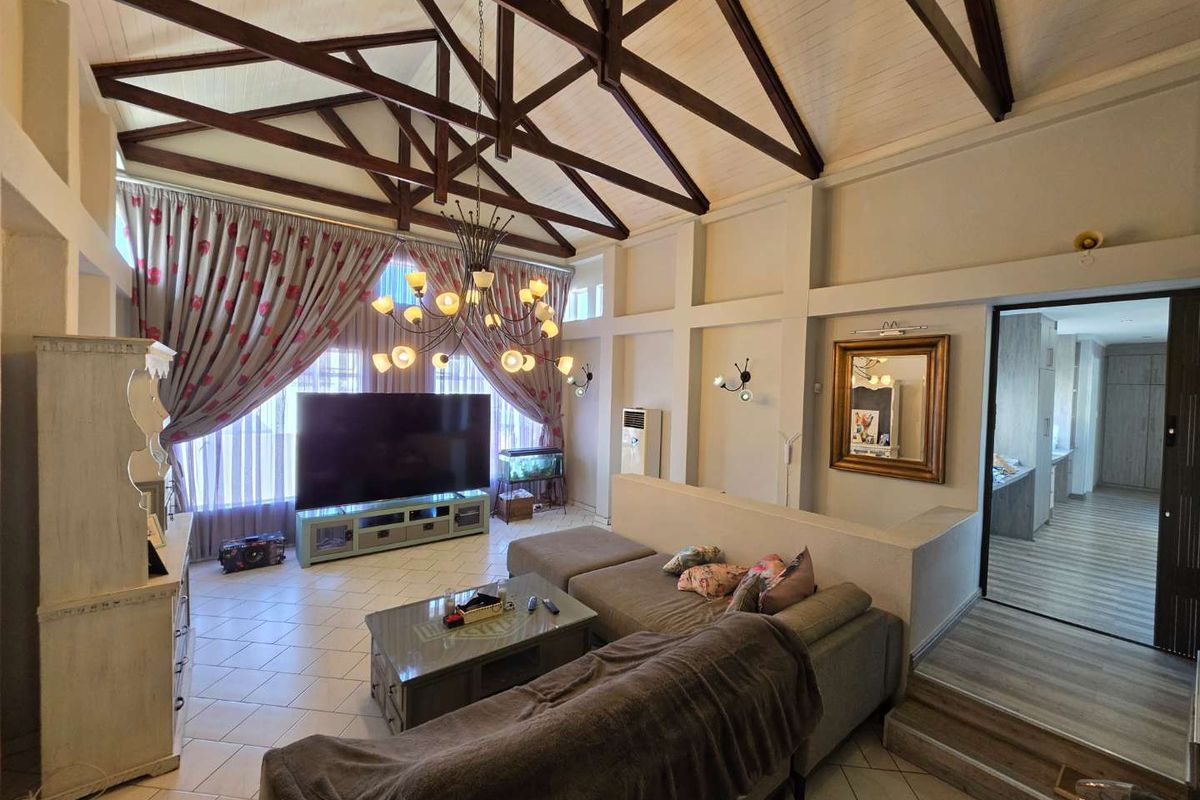 Spacious living area featuring high vaulted ceilings with exposed timber trusses, tiled flooring, and a semi-open plan layout leading to an adjacent room.