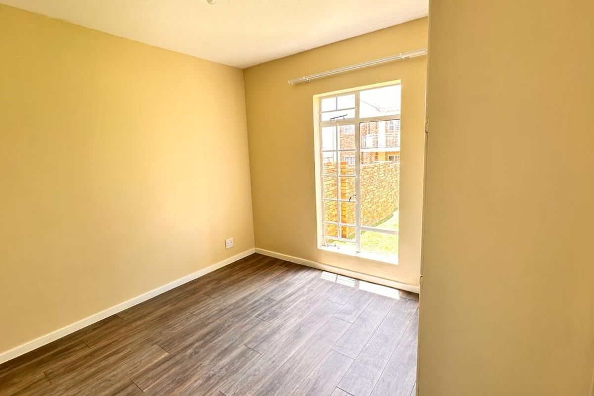 A bright, empty bedroom featuring modern laminate flooring, neutral wall paint, and a large window allowing for ample natural light.