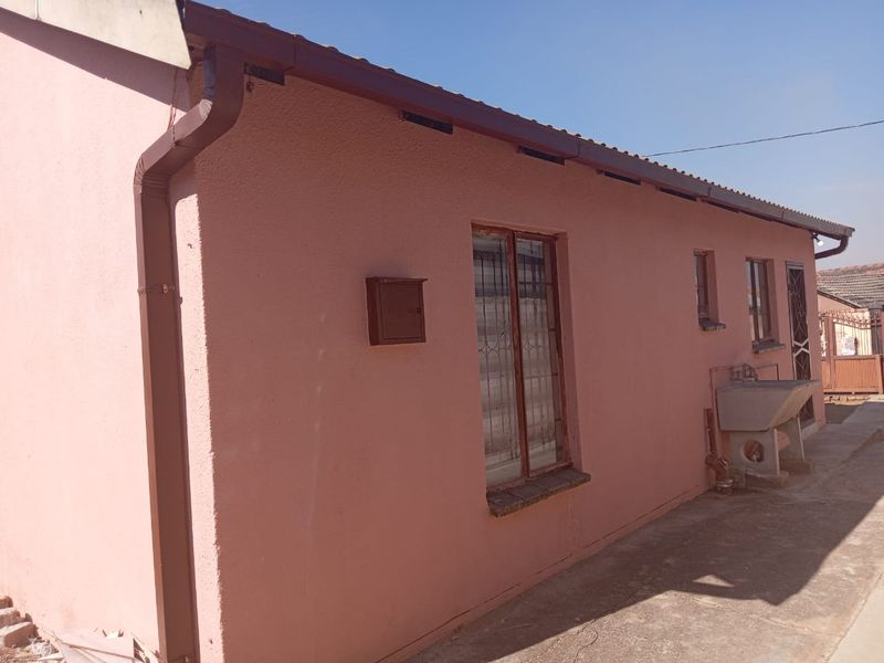 Rear exterior view of the house featuring a concrete utility sink, security bars on windows, and paved walkway area.