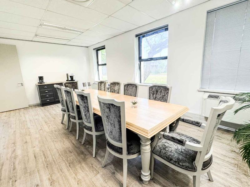 A professional office meeting room featuring laminate flooring, a suspended ceiling with recessed lighting, and large windows with venetian blinds.