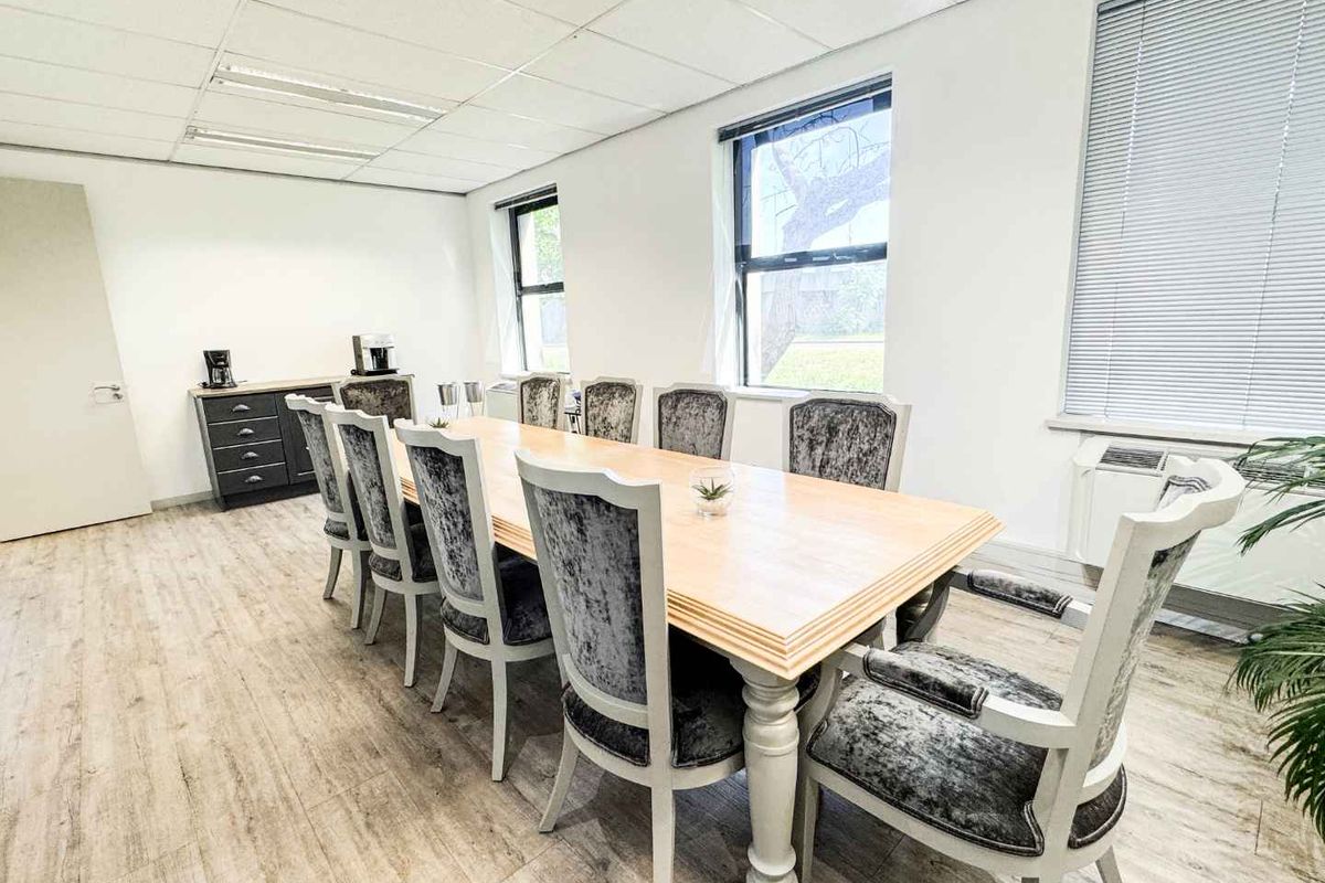 A professional office meeting room featuring laminate flooring, a suspended ceiling with recessed lighting, and large windows with venetian blinds.