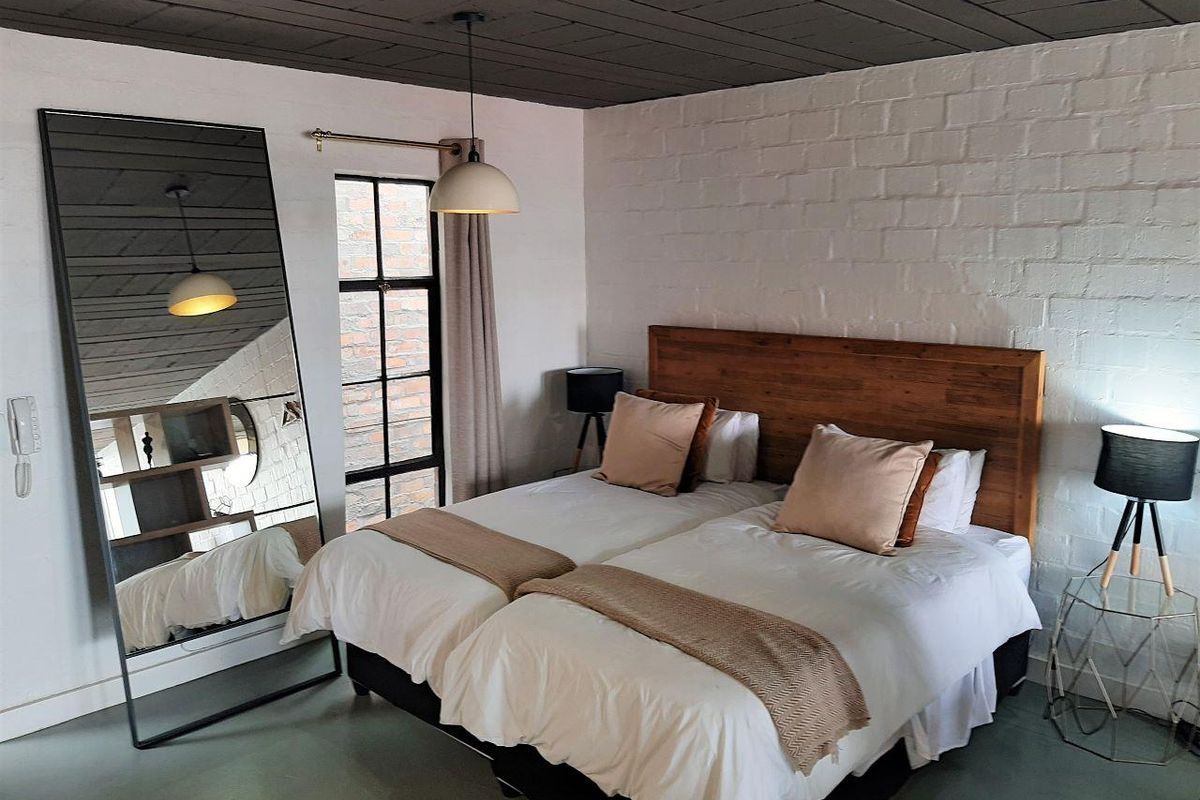 A well-maintained bedroom featuring a textured white brick wall, dark timber ceiling, and a large steel-framed window providing natural light.