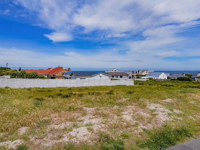 A vacant residential plot featuring a precast concrete boundary wall, offering a clear view of the surrounding neighborhood and distant coastal horizon.