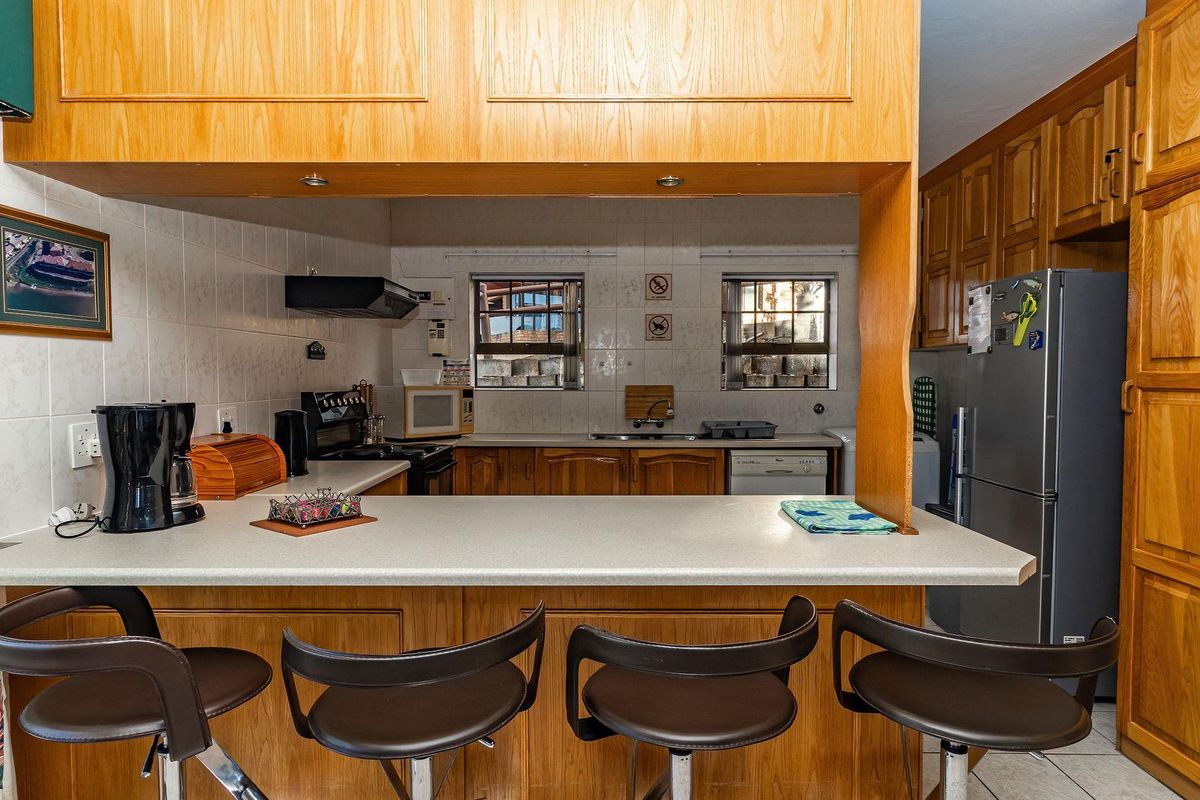 A functional kitchen featuring wooden cabinetry, a breakfast bar counter, tiled splashbacks, and built-in appliances, offering a traditional layout.