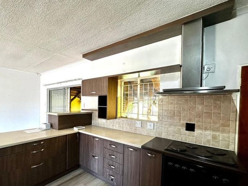 A functional kitchen featuring dark laminate cabinetry, light countertops, a tiled backsplash, and integrated stainless steel appliances.