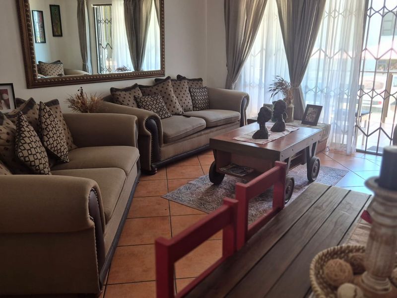 A comfortable living room featuring tiled flooring, a large wall mirror, and sliding glass doors with security gates leading to the exterior.