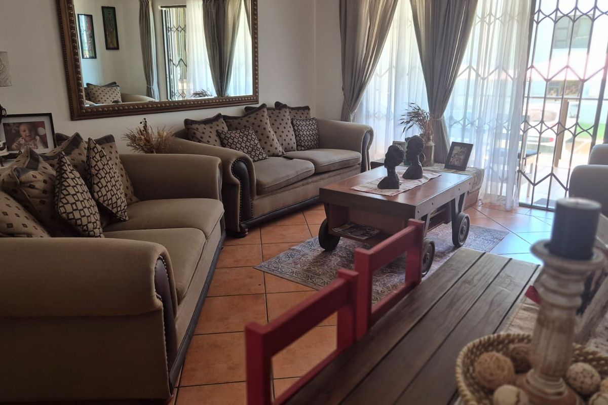 A comfortable living room featuring tiled flooring, a large wall mirror, and sliding glass doors with security gates leading to the exterior.