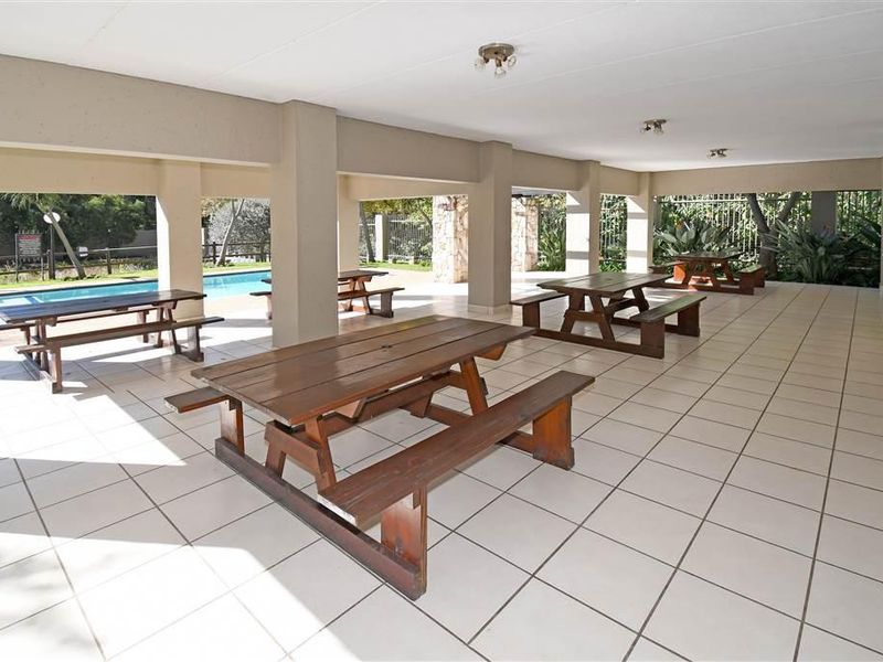 A spacious covered outdoor entertainment area featuring tiled flooring, concrete pillars, and direct access to a swimming pool.