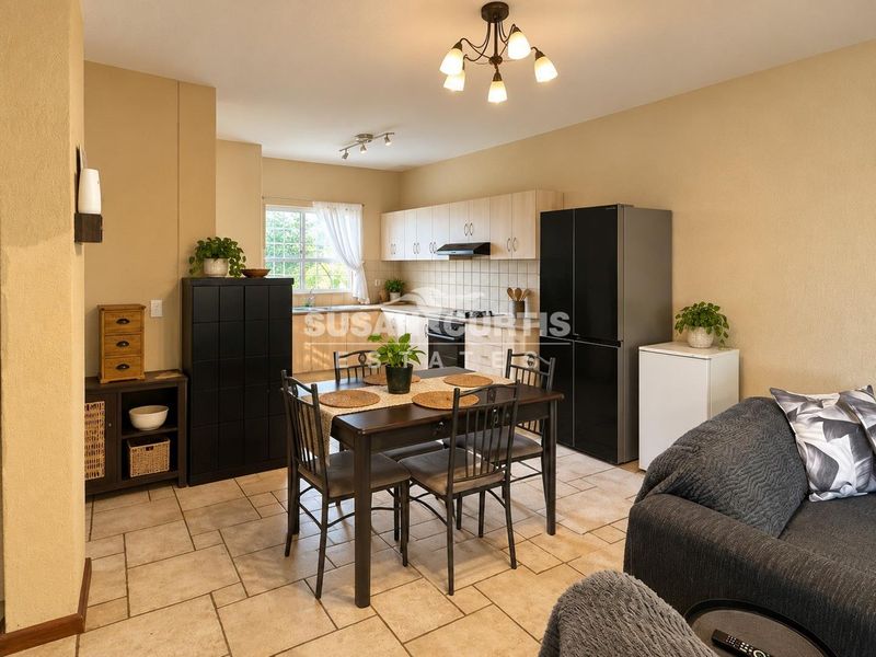 Open-plan living and dining area featuring a functional kitchen with built-in cabinetry, tiled flooring, and a neutral color palette.
