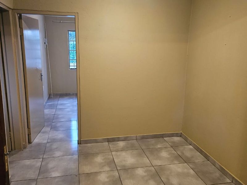 An empty, neutrally painted living area featuring tiled flooring, ceiling cornicing, and a doorway leading to an adjacent room.