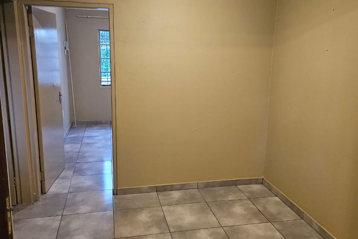 An empty, neutrally painted living area featuring tiled flooring, ceiling cornicing, and a doorway leading to an adjacent room.