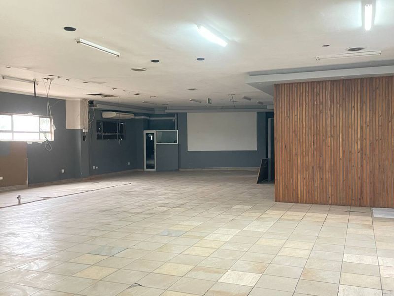 A large, vacant open-plan industrial space featuring tiled flooring, timber wall paneling, and fluorescent lighting, currently requiring maintenance and cosmetic updates.